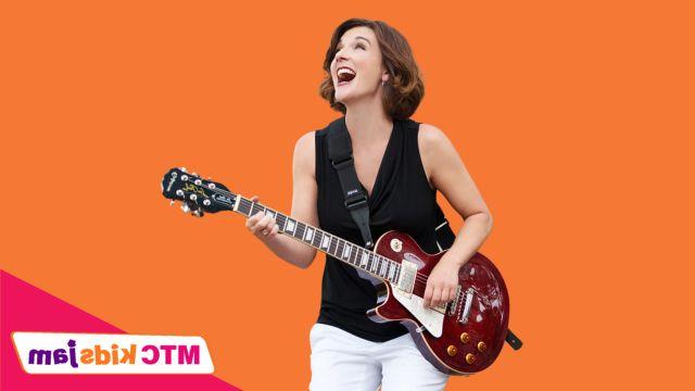 Krista Tatschl Eyler拿着吉他微笑着. 她站在橙色的背景下.